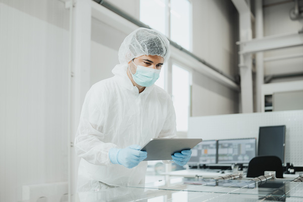Prüfingenieur im Reinraumanzug prüft ein Substrat und hält ein Tablet in den Händen