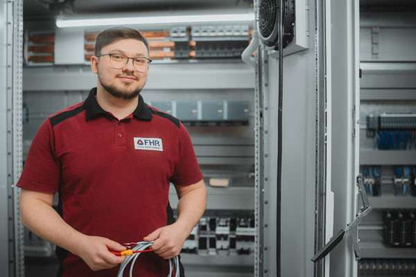 Eletriker steht vor einem Schaltschrank und h&auml;lt Kabel vor sich